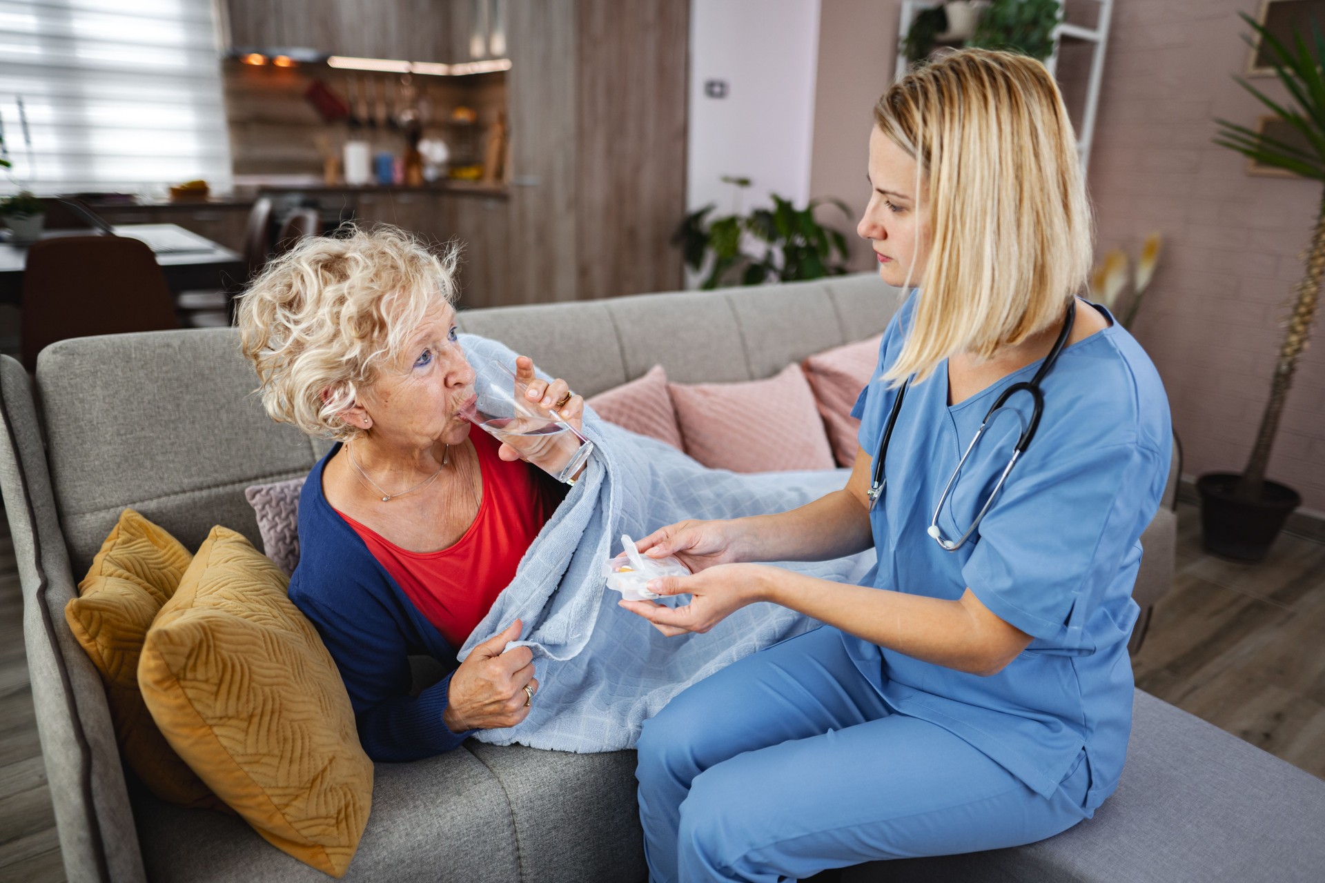 Caring nurse assists elderly woman with medication at home during day