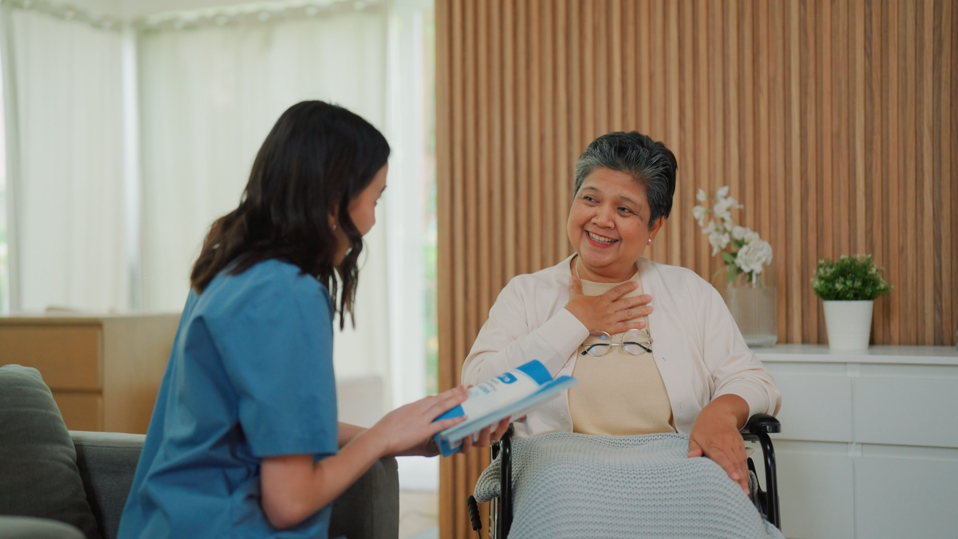 Young Asian nurse talking casually with senior patient while providing medicare service.