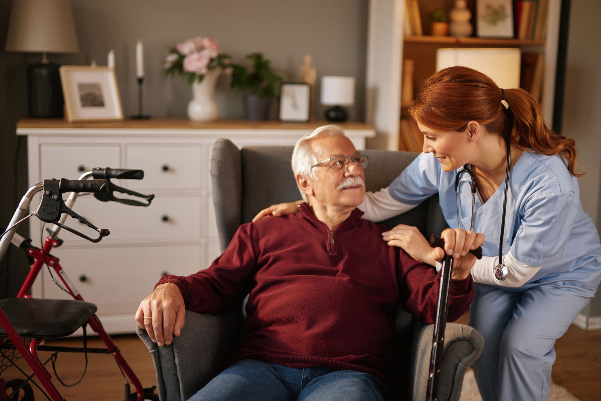 Nurse assisting elderly man at home with walking cane